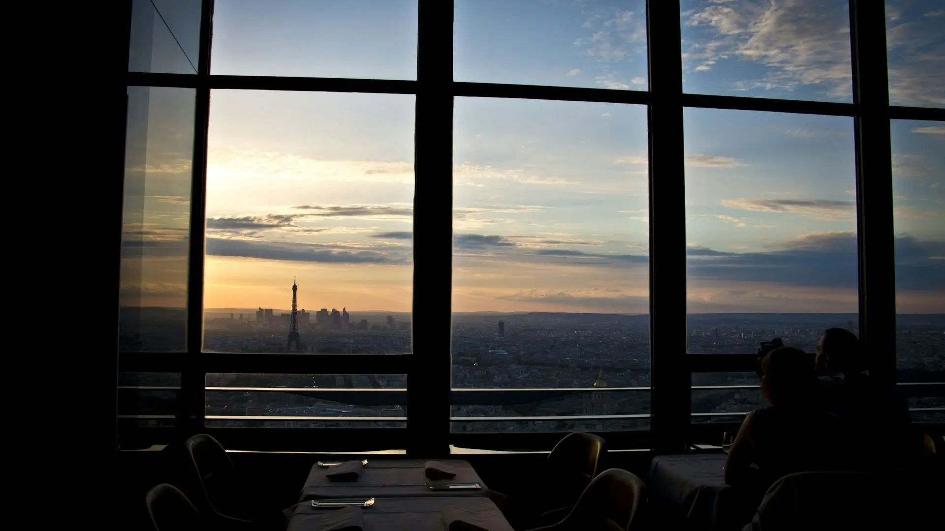 Dining table by a large window with the Eiffel Tower on the horizon at dusk Dining table by a large window with the Eiffel Tower on the horizon at dusk